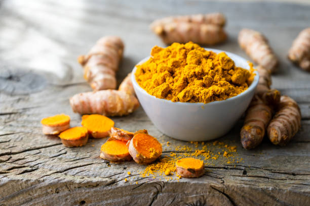 A bowl of turmeric powder and turmeric roots on a wooden surface, illustrating the source of stains.