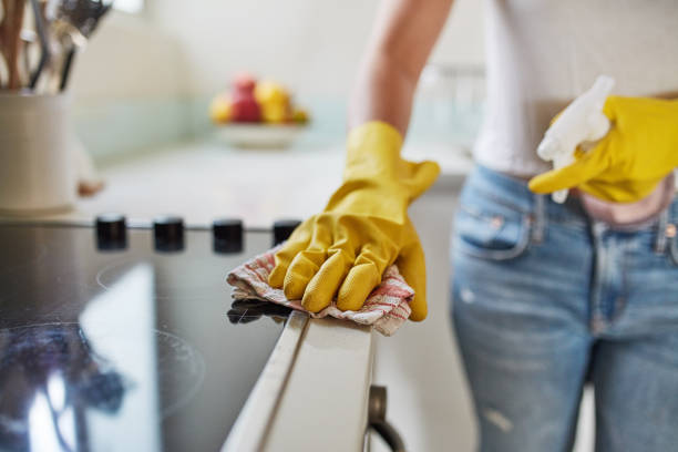 Person wearing yellow gloves cleans kitchen stove with a cloth, making tidying up easier.